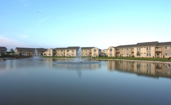 a fountain in the middle of a lake with a row of houses in the background