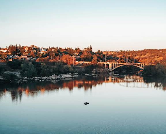 A serene lake with a bridge in the background and a small boat floating on the water.