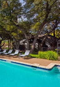 a swimming pool with chaise lounge chairs and trees in the background
