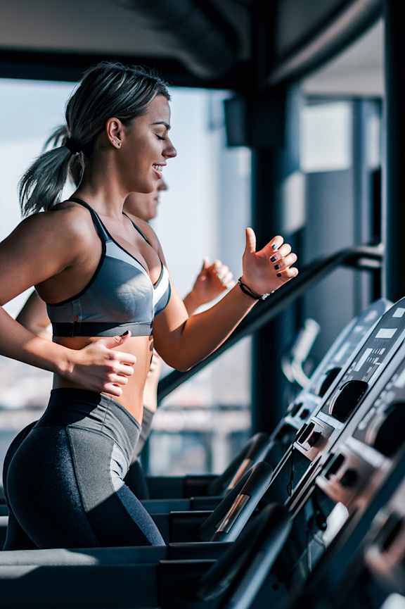 A woman is running on a treadmill in a gym.