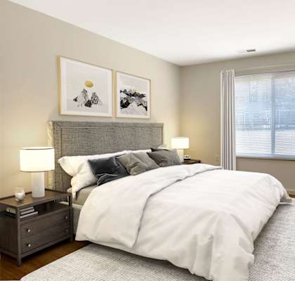 A bedroom with a large bed, a nightstand with a lamp, and a dresser with a vase of flowers.