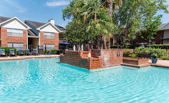 A swimming pool in front of a brick building with a fountain in the middle.
