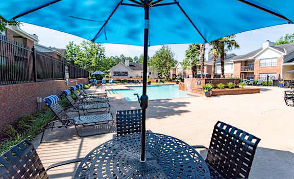 A blue umbrella shades a table in a sunny courtyard.