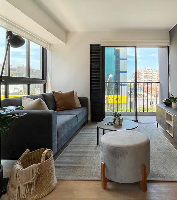 A living room with a grey couch, a round ottoman, and a wooden coffee table.