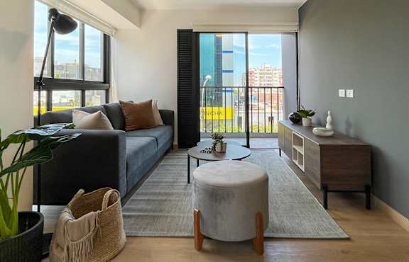 A living room with a grey couch, a round ottoman, and a wooden coffee table.