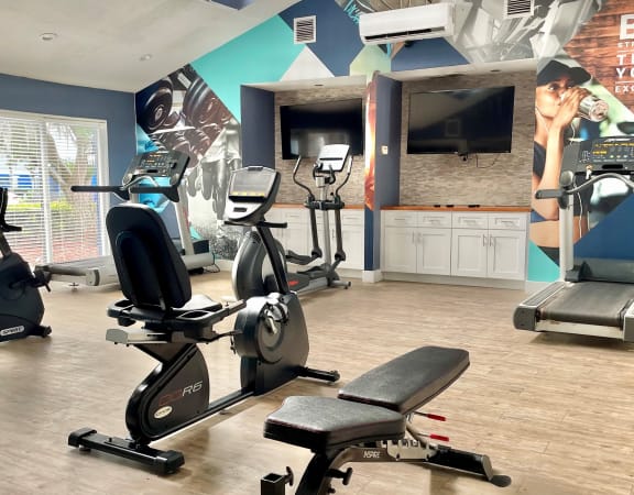 a gym with cardio machines and a tv
