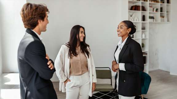 Three people in business attire are standing in a room.