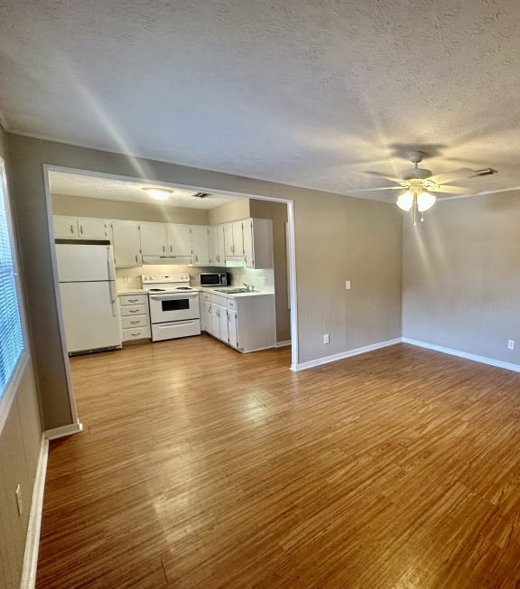 an empty living room and kitchen with wood floors and a ceiling fan