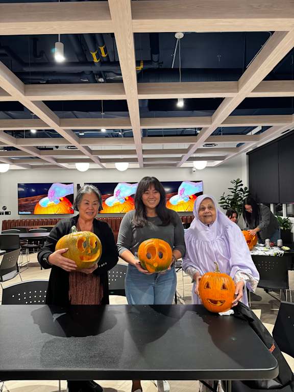 Three people holding pumpkins in an office setting.