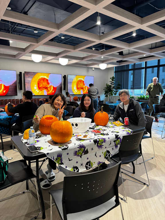 A group of people are sitting around a table with pumpkins on it.
