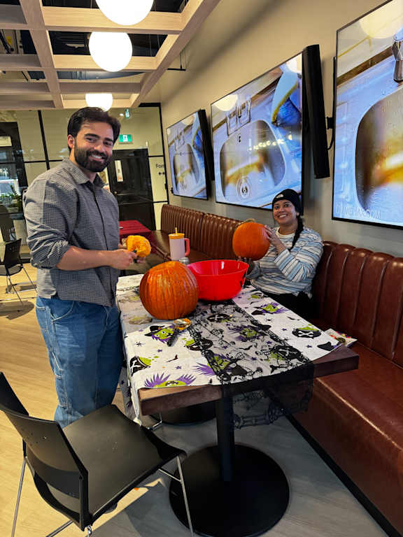 A man and a woman are sitting at a table with a pumpkin in front of them.