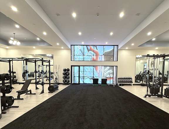 A gym with a variety of equipment and a large screen on the wall.