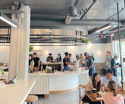 A group of people are sitting and standing around a counter in a modern cafe. at Main+Nine, Riverside, 92501