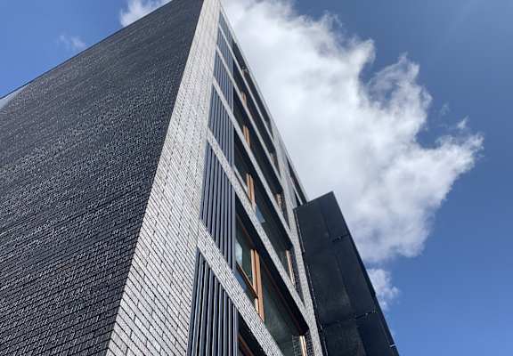 A tall building with a black facade and a blue sky with clouds in the background.