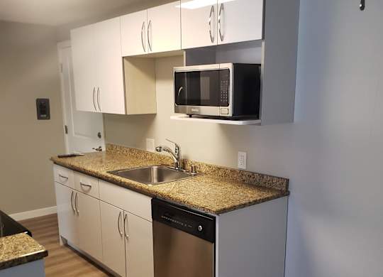 a small kitchen with white cabinets and a wooden floor