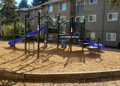 a playground with a blue slide in front of an apartment building