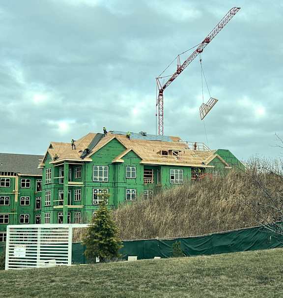 A green building under construction with a crane in the background.