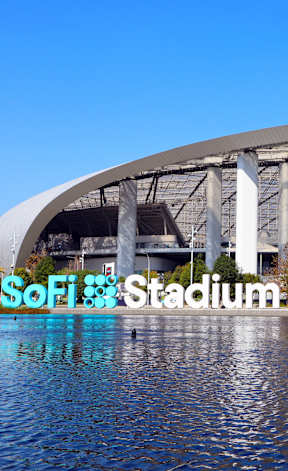 A large stadium with a semi-circular roof and a body of water in the foreground.