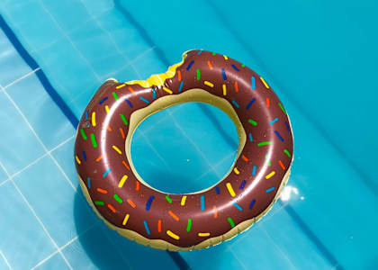 A chocolate donut with sprinkles is floating in a pool.