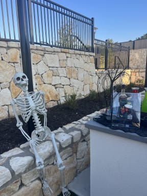 a skeleton sitting on a wall next to a flower garden