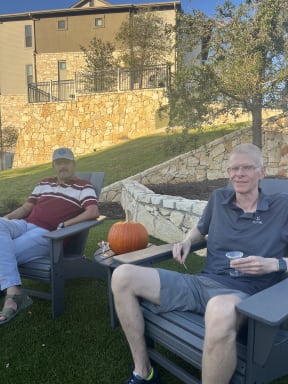 two men sitting on chairs in the lawn with a pumpkin
