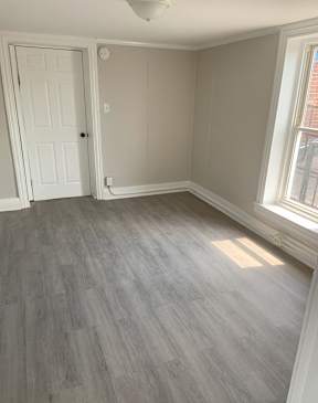 A room with a white door and a window with a grey floor.