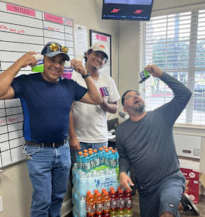 three men pose with bottles of soda in an office