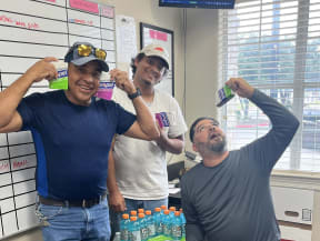 three men pose with bottles of soda in an office