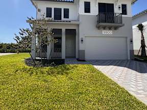 A white house with a dark roof and a tree in front of it.