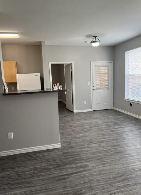 an empty living room with a kitchen and a white door