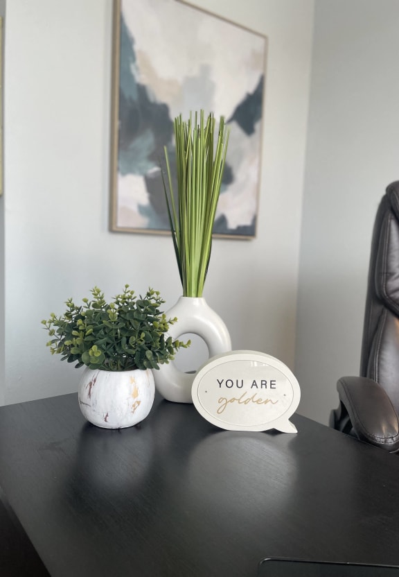 a desk with a vase with plants and a sign that says you are green