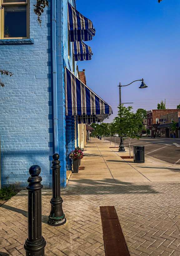 A blue building with a striped awning is on the corner of a street.