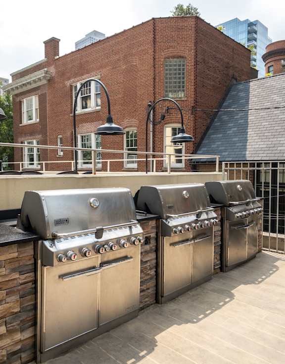 A row of four built in BBQ grills on a balcony.