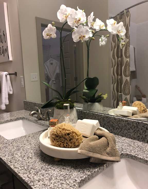 A bathroom sink with a bowl of sponges and a vase of flowers.