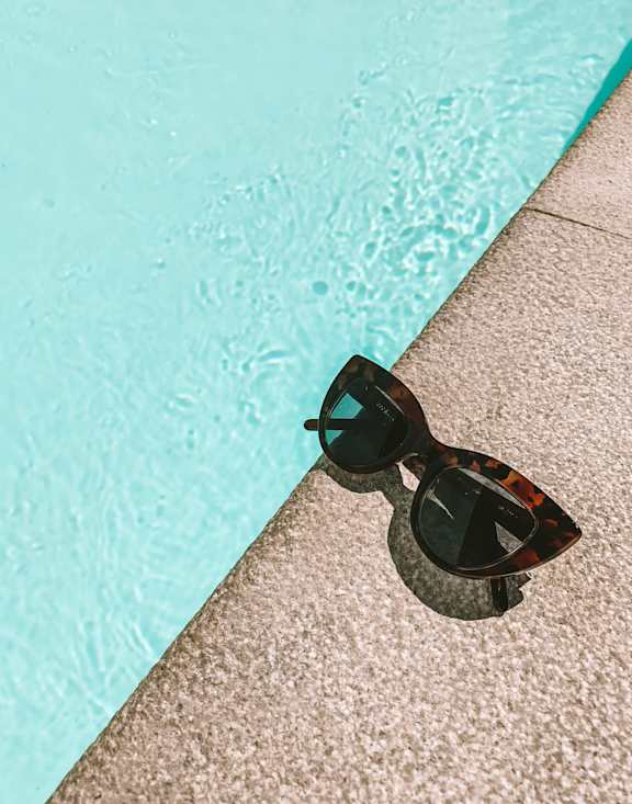 A pair of sunglasses is reflected in a pool.