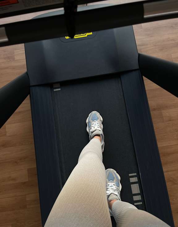 A person is running on a treadmill with grey sneakers and beige pants.