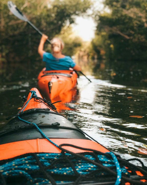 a woman kayaking down a river in a orange kayak