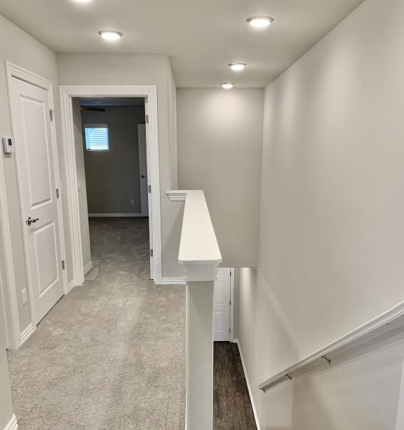 a finished basement with a landing with a staircase and a hallway with white walls