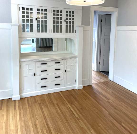 A white cabinet with a window and drawers is in a room with wooden floors.