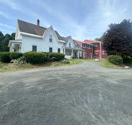A white house with a red roof is situated in front of a green tree at Briarcliff at Quechee Apartments, Vermont