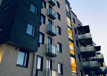 A tall building with balconies and windows is shown against a blue sky.