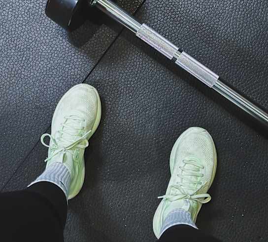 A person is standing on a black floor with a barbell on their feet.