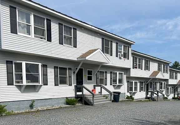 A gravel parking lot in front of a building with a white and grey facade. at Briarcliff at Quechee Apartments, Vermont
