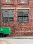 A green generator sits in front of a brick wall with a window.