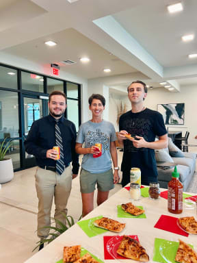 three men standing in front of a table with pizza and drinks