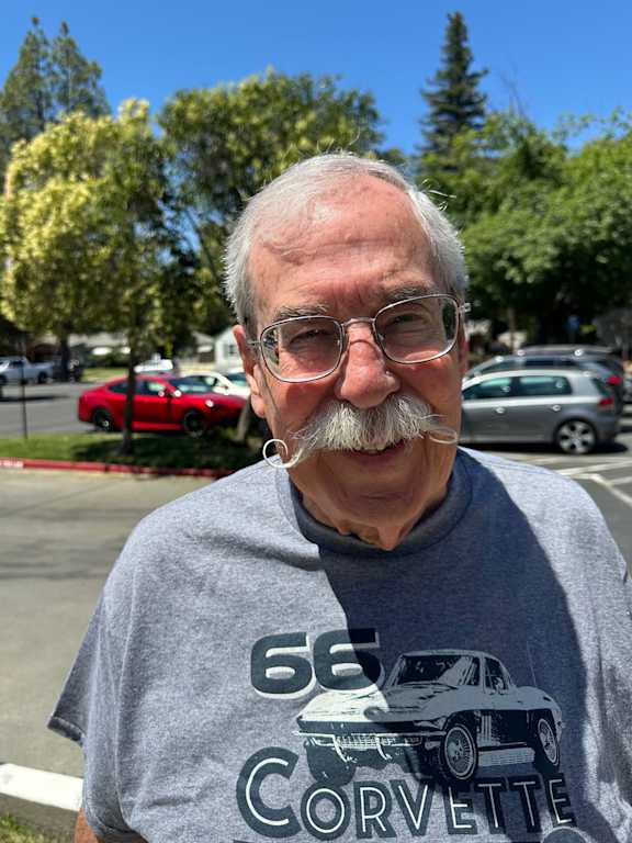 A man with a Corvette t-shirt standing in a parking lot.