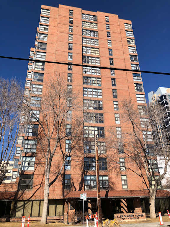 A tall red brick building with many windows and a tree in front of it.