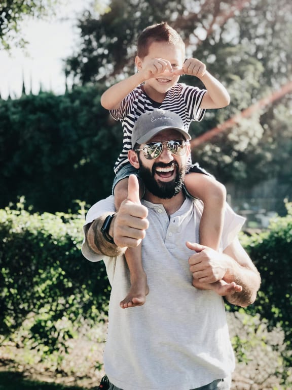 a man holding a child on his shoulders and giving a thumbs up