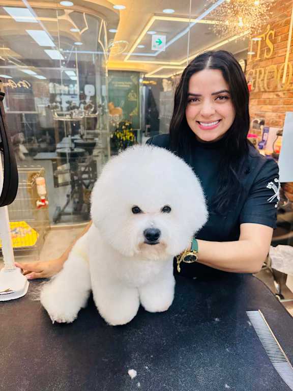A woman with a black shirt is holding a white dog in a grooming salon.