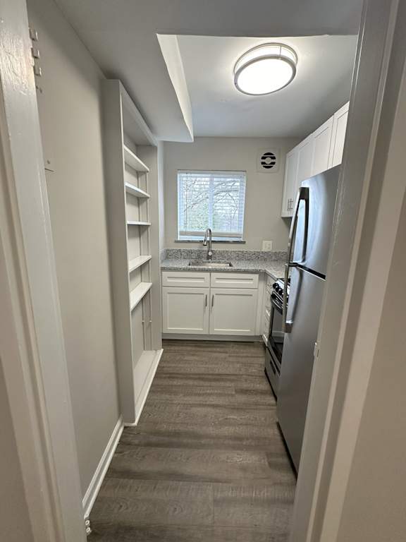 A narrow kitchen with white cabinets and a refrigerator.